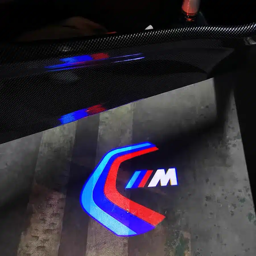 BMW M Sport Door Lights Close-up of BMW 3M Sport door lights casting bright emblem on ground in low-light UK setting